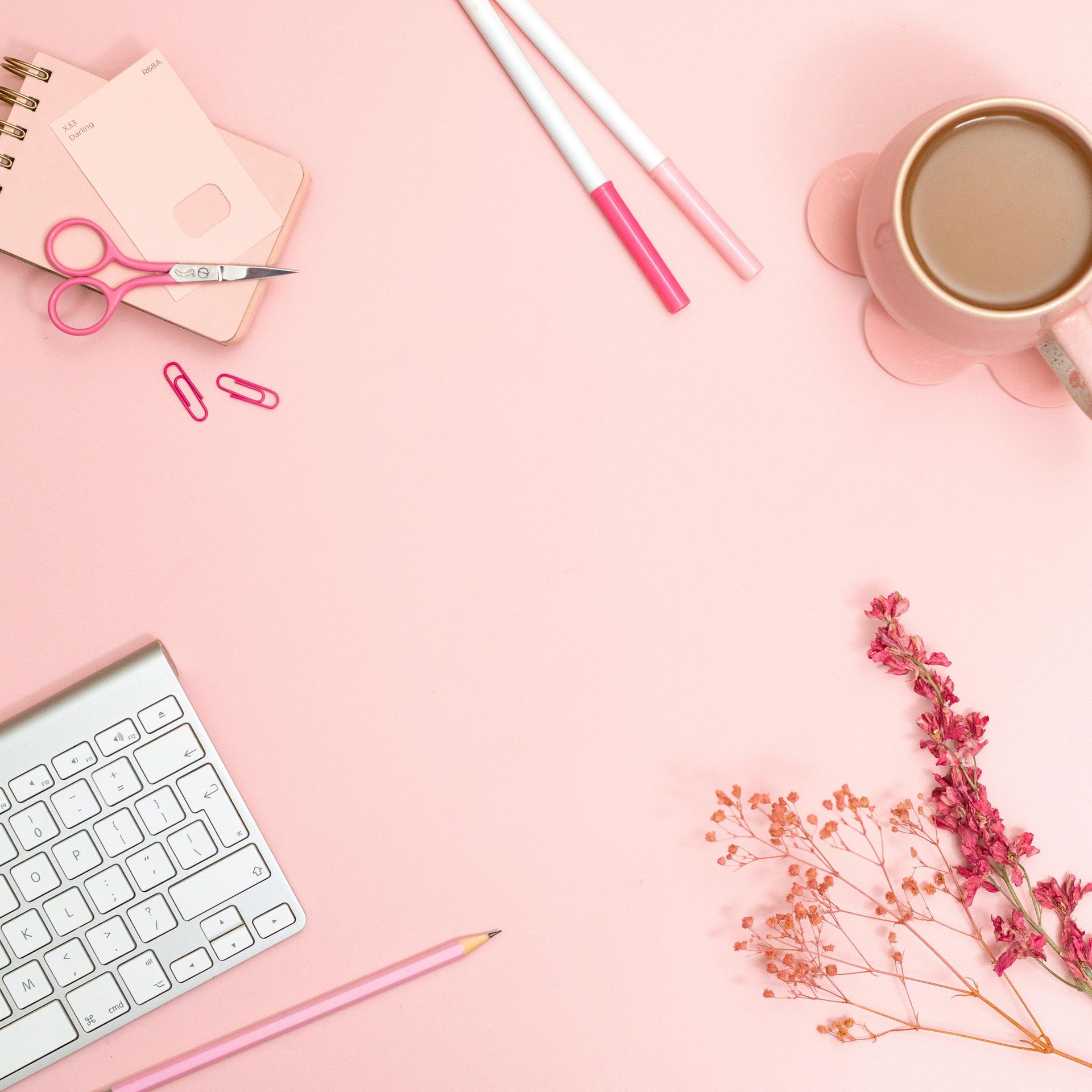 Minimalist pink desk flat lay featuring stationery, keyboard, and coffee for a creative workspace vibe.